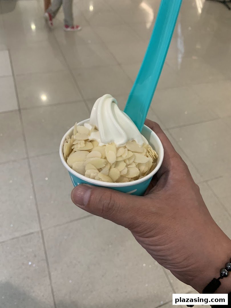 A hand holds a cup of Yolé frozen yogurt topped with almond flakes and a blue spoon.