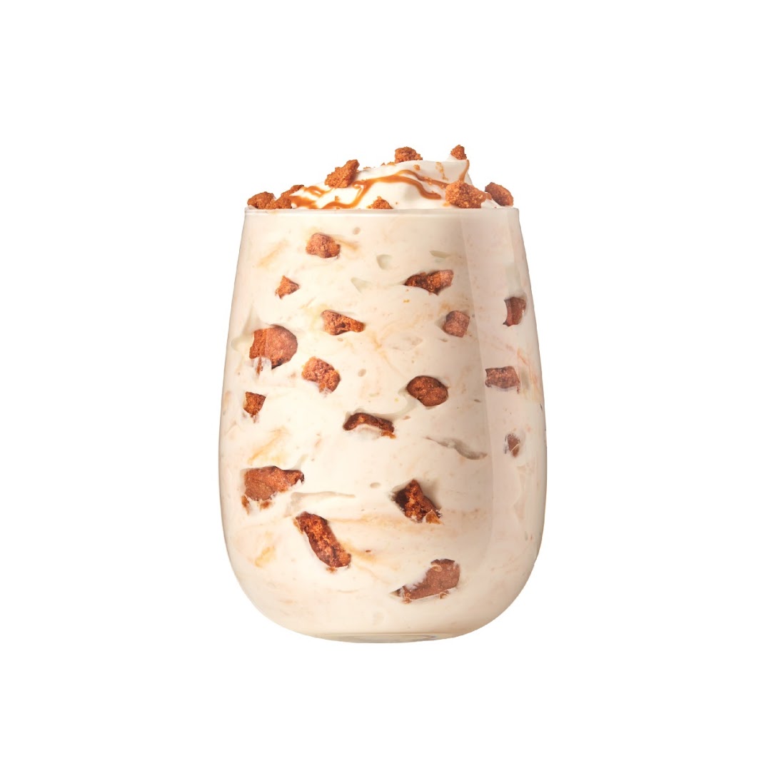 A creamy dessert in a glass, topped with caramel drizzle and crunchy biscuit pieces.