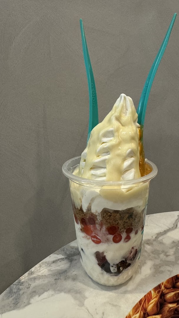A delicious layered frozen yogurt dessert with toppings and two spoons in a clear cup.
