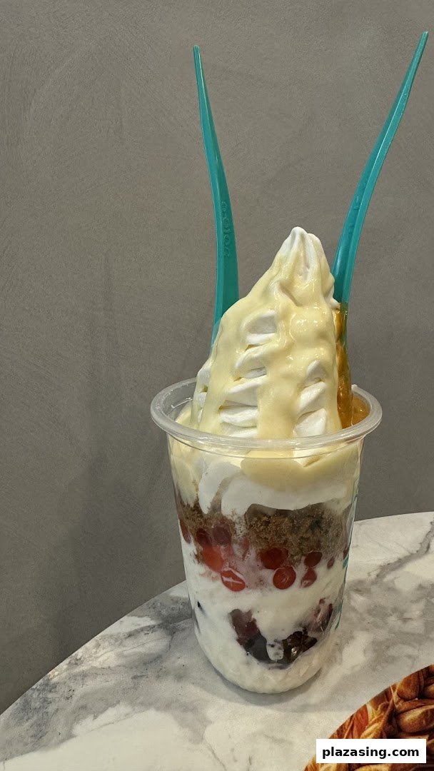 A delicious layered frozen yogurt dessert with toppings and two spoons in a clear cup.