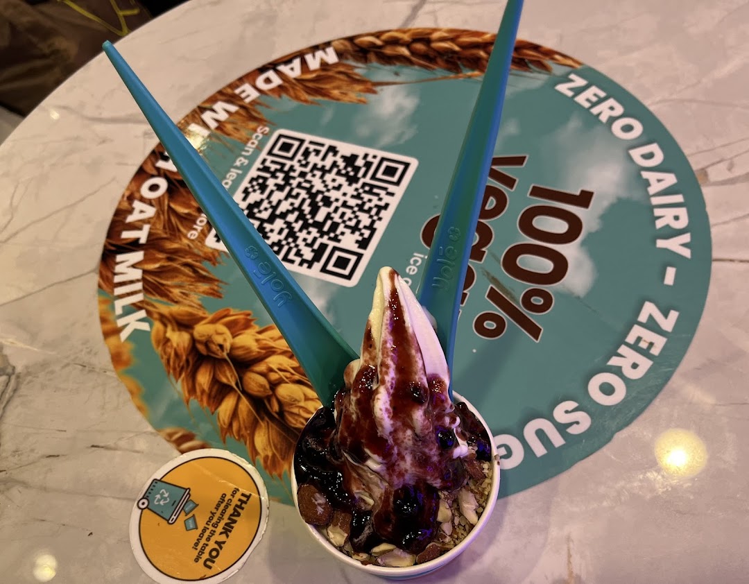A Yolé frozen yogurt cup with toppings and spoons on a branded placemat featuring oat milk and zero dairy.