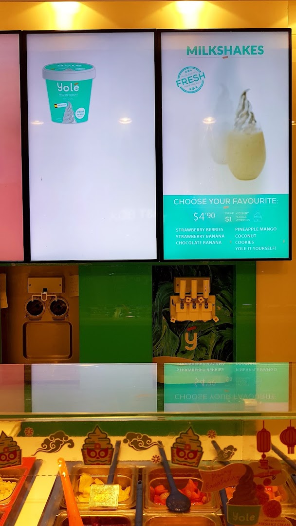 Digital menu boards for Yolé frozen yogurt and milkshakes, with a vibrant toppings bar visible below.