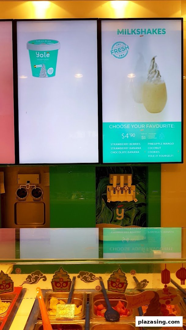 Digital menu boards for Yolé frozen yogurt and milkshakes, with a vibrant toppings bar visible below.