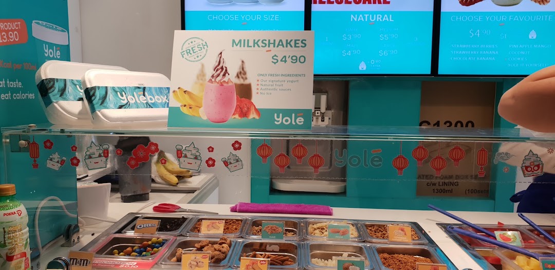A vibrant Yolé frozen yogurt counter showcasing various toppings, milkshakes, and digital menu displays.