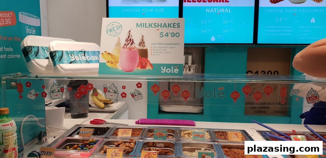 A vibrant Yolé frozen yogurt counter showcasing various toppings, milkshakes, and digital menu displays.