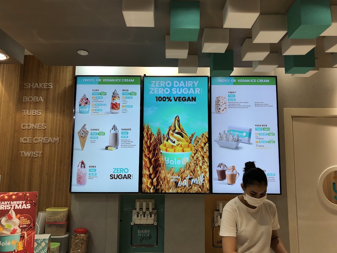 Digital menu boards at Yolé Plaza Singapura displaying various froyo, shakes, and vegan ice cream options.