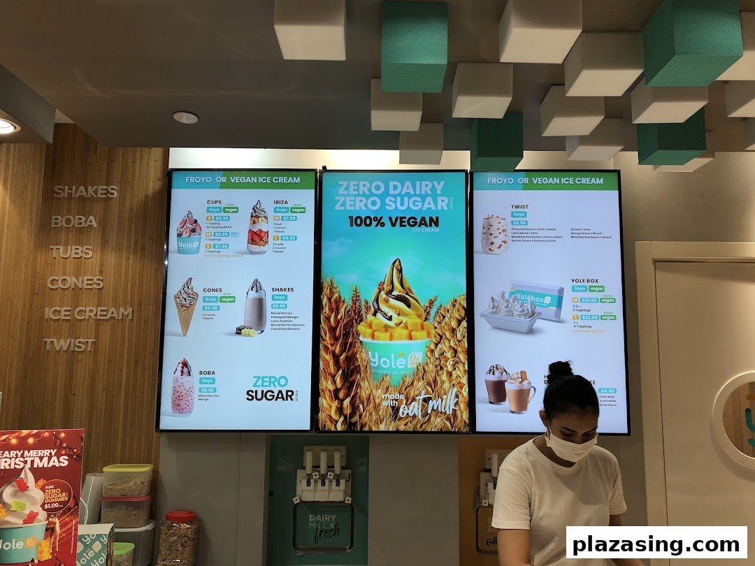 Digital menu boards at Yolé Plaza Singapura displaying various froyo, shakes, and vegan ice cream options.