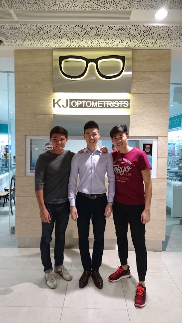 Three friendly staff members stand proudly in front of the KJ Optometrists shop sign.