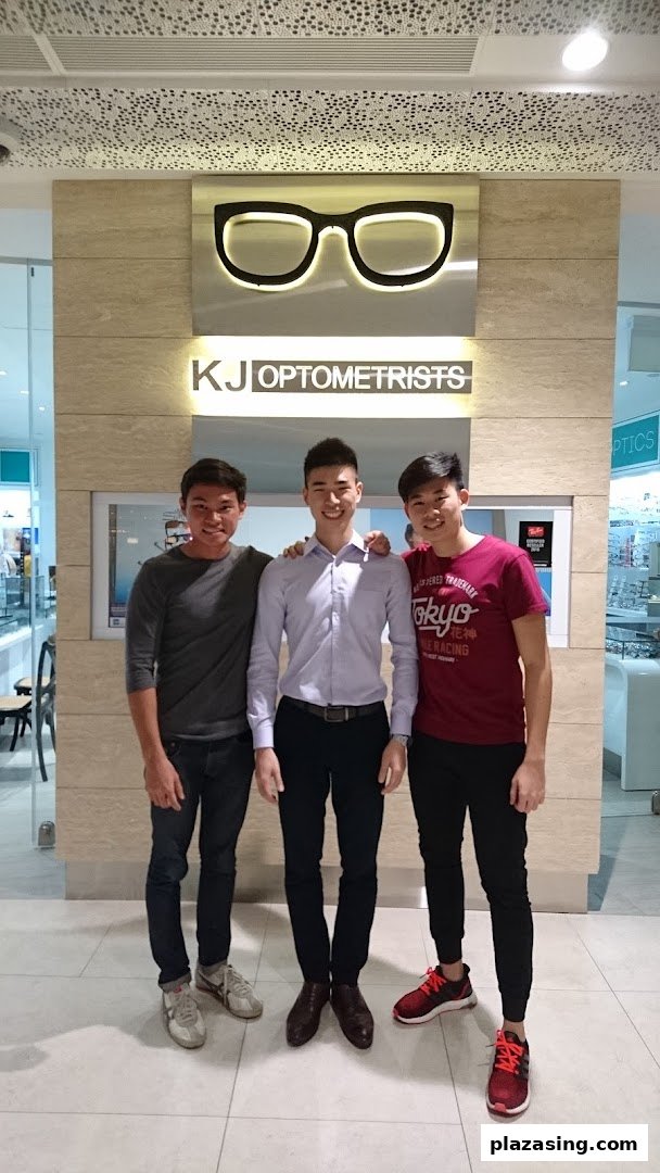 Three friendly staff members stand proudly in front of the KJ Optometrists shop sign.