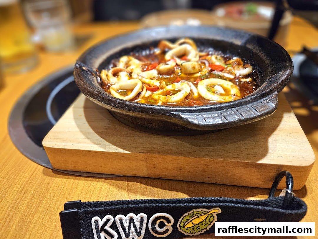 A close-up shot of a claypot dish with squid rings and vegetables, served on a wooden stand.