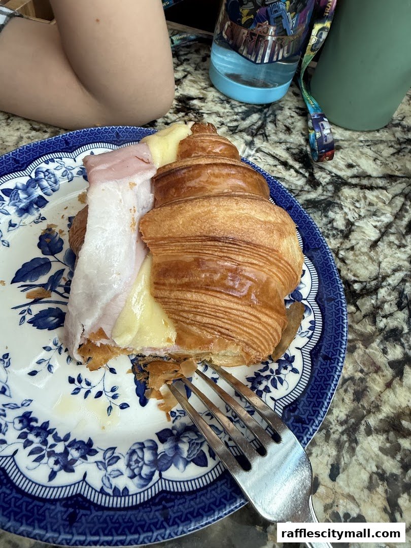 A ham and cheese croissant on a blue and white floral plate with a fork.