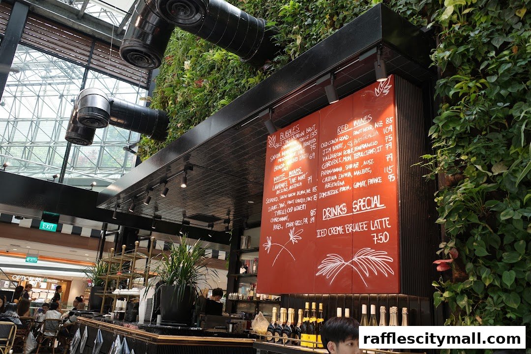 A red menu board with drinks and wine selections is displayed in a cafe with a living green wall.