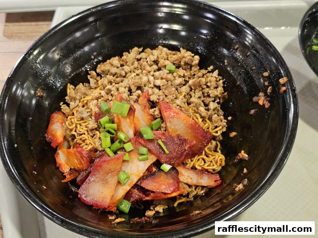 A close-up of a bowl of noodles topped with char siu and minced meat, garnished with spring onions.