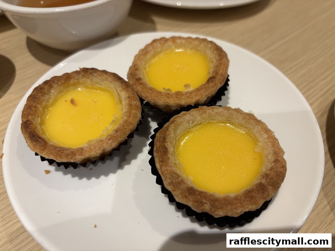 Three golden-brown egg tarts with creamy yellow filling on a white plate.