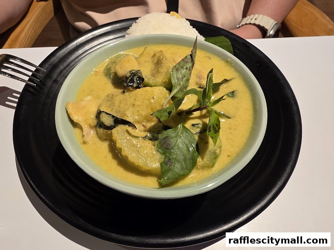 A bowl of Thai green curry with chicken and rice, garnished with basil leaves.