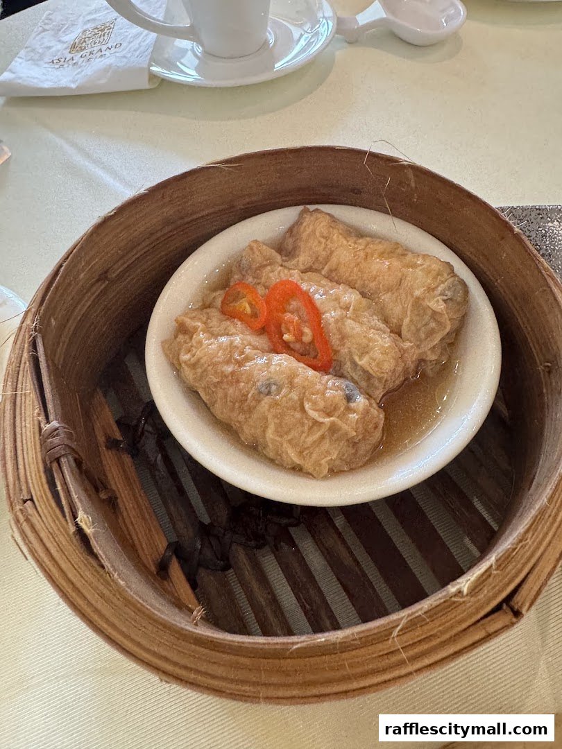 A close-up of a bamboo steamer basket filled with fried tofu skin rolls topped with chili.