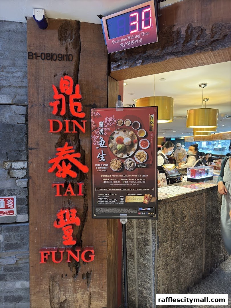 The entrance of Din Tai Fung restaurant with a waiting time display and a promotional poster.