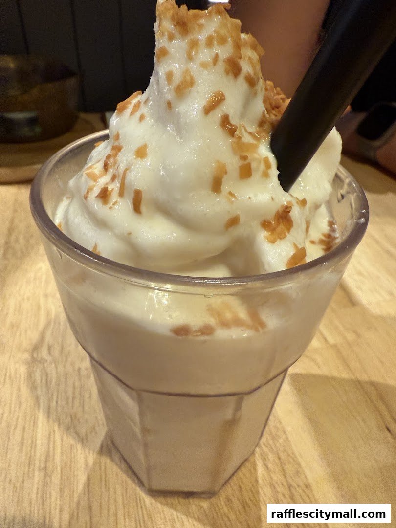 A close-up of a creamy dessert topped with crunchy bits and a black straw.