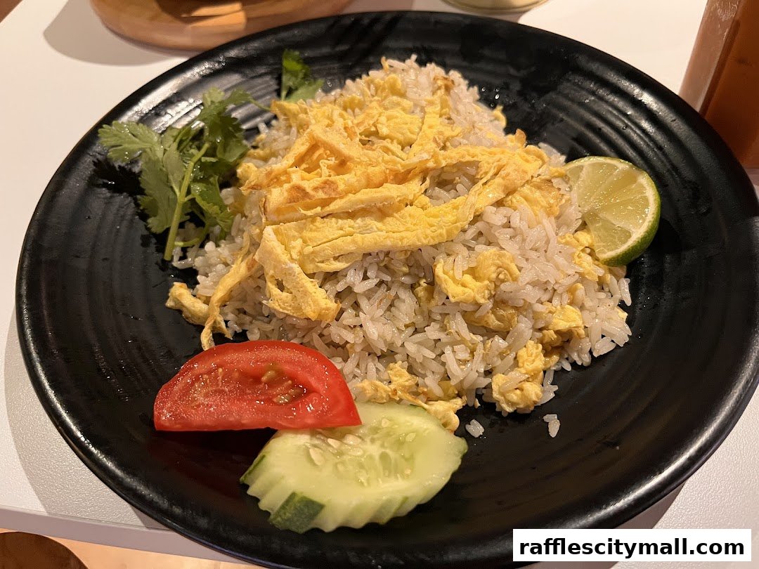 A plate of Thai fried rice with scrambled egg, lime, tomato, and cucumber.