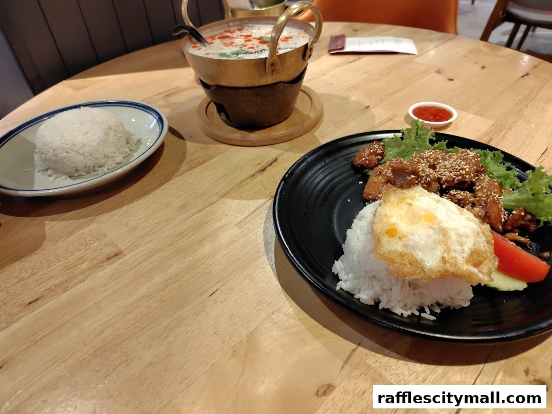 A table setting with Thai food, including rice, a soup, and a main dish with a fried egg.