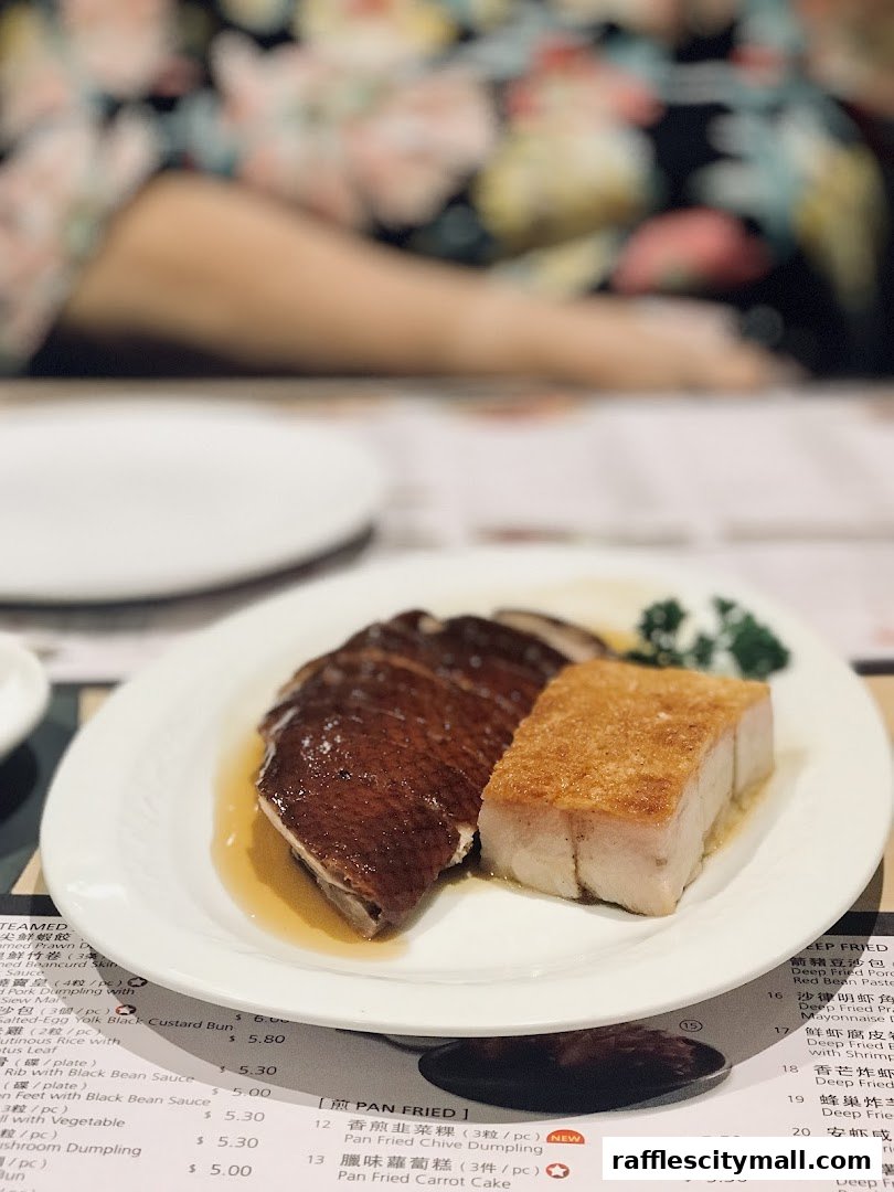 A plate of roasted duck and crispy pork belly sits on a table with a menu.