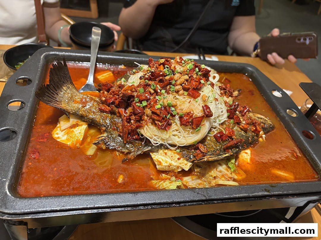A close-up of a spicy claypot fish dish with noodles and chili peppers.