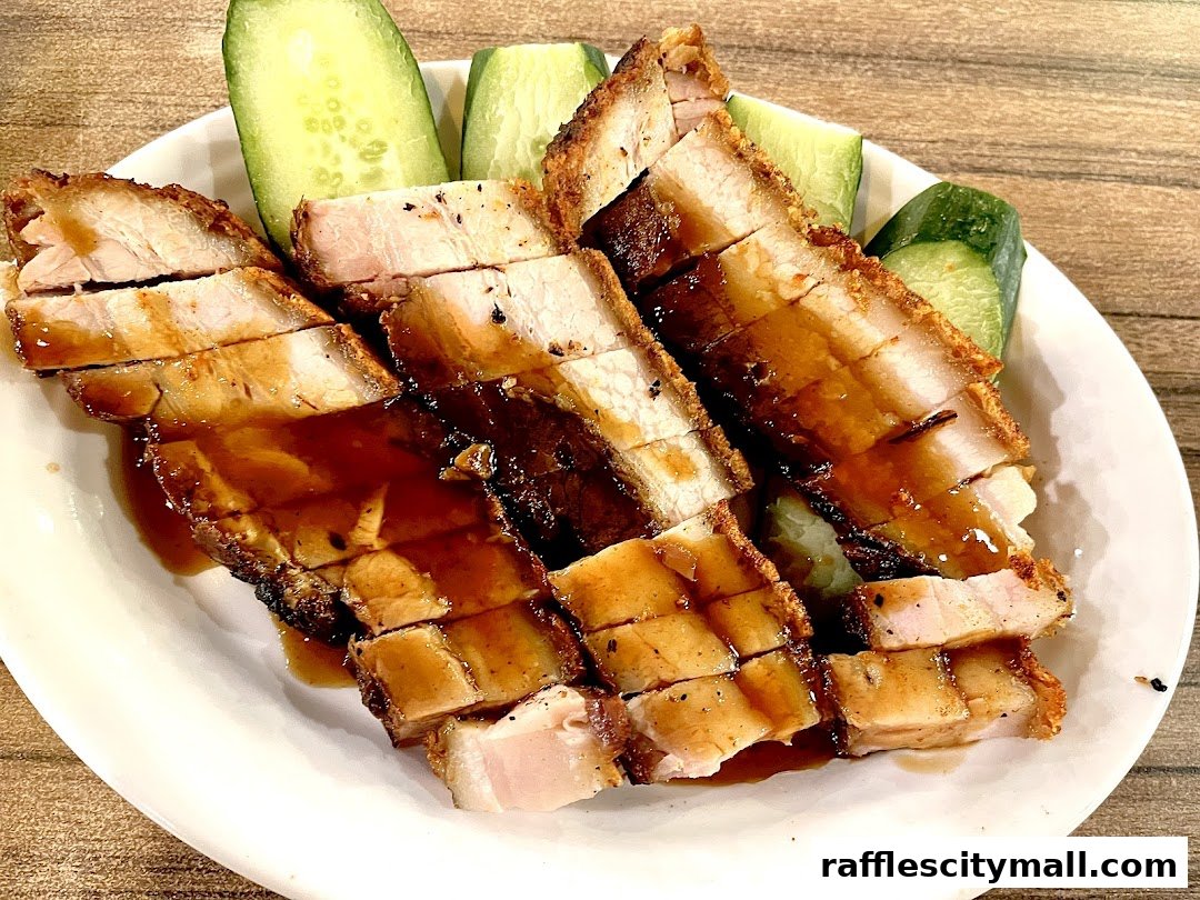 A plate of crispy roasted pork belly with a savory sauce and cucumber slices.