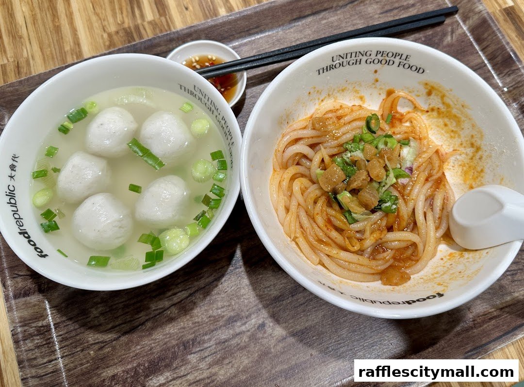 A close-up of two bowls of noodles and fish balls, served with chopsticks and dipping sauce.