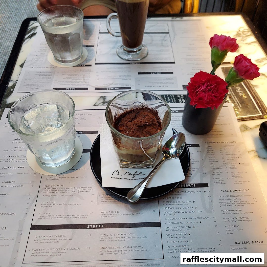 A table setting at PS.Cafe Raffles City with two glasses of water, a dessert, and a coffee drink.