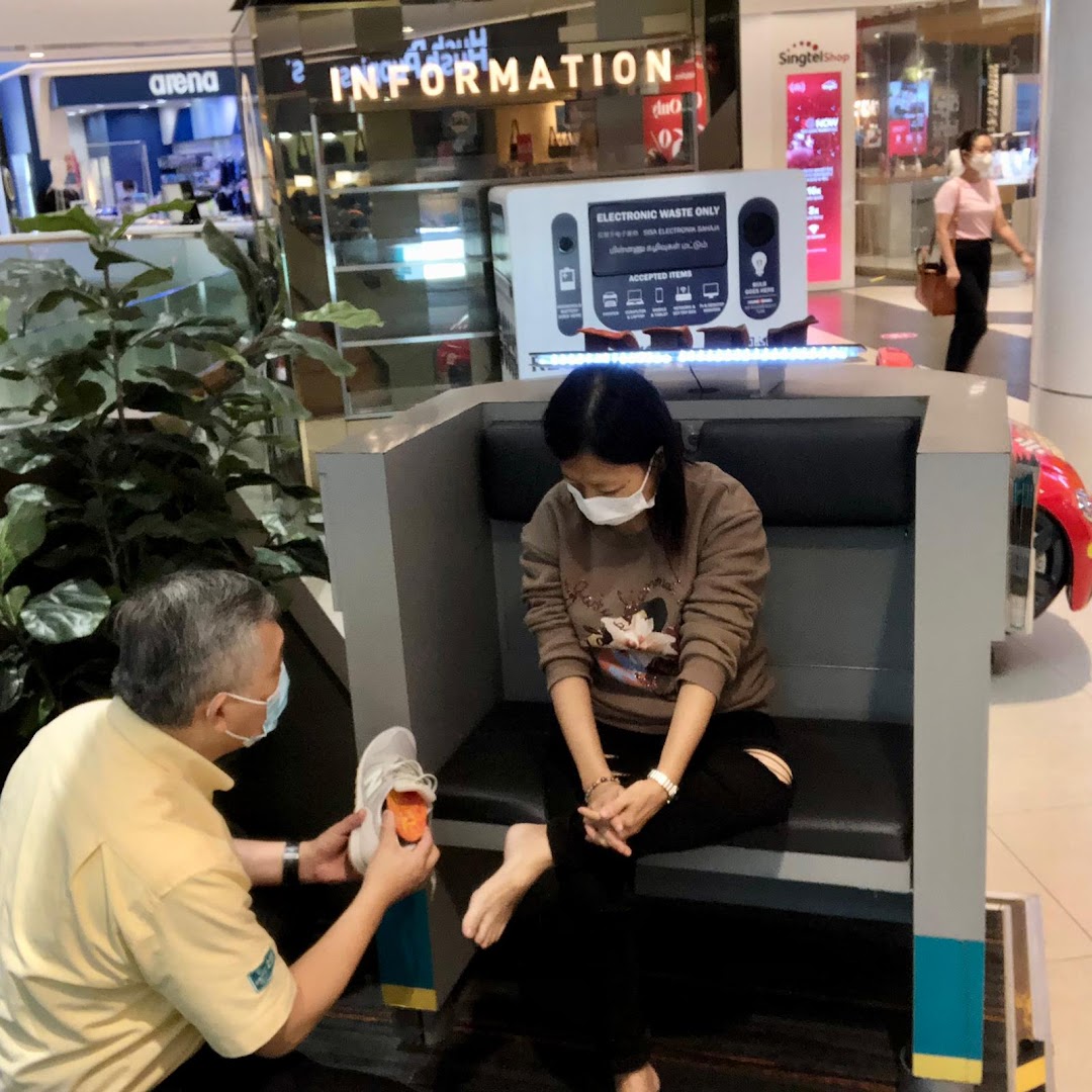 A staff member assists a customer with an orthotic fitting in a mall setting.