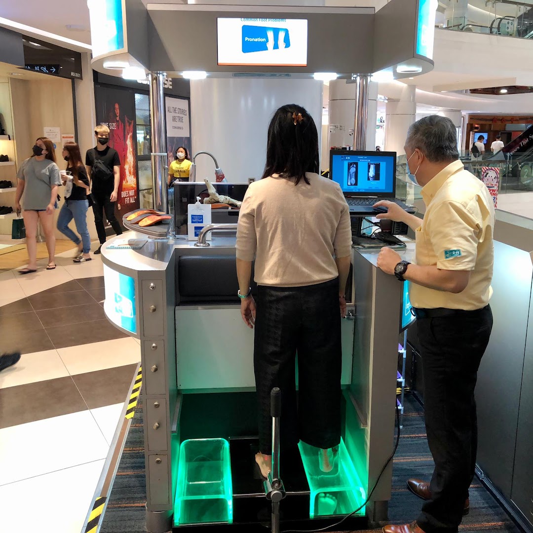 A customer receives a foot scan at a 2ft Orthotics station, assisted by a staff member.