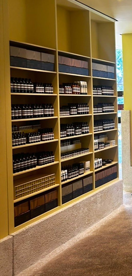 A well-organized display of Aesop skincare and body care products on yellow shelves inside the store.
