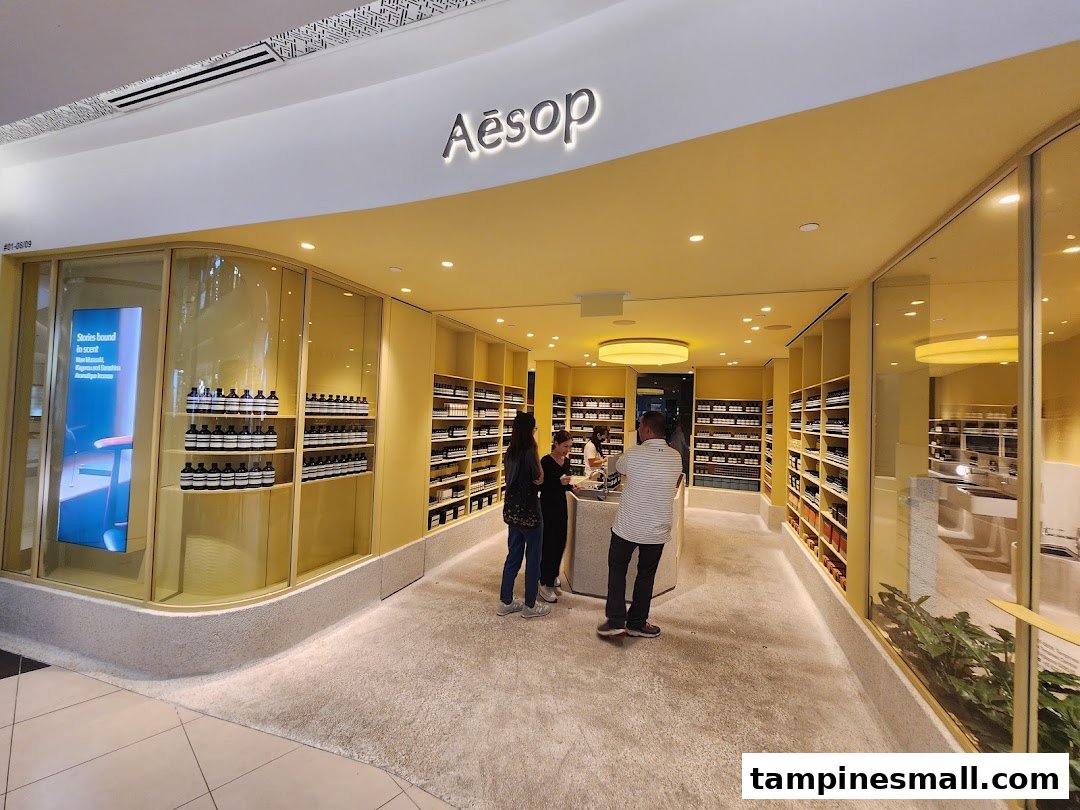 The Aesop store entrance features a warm yellow interior, displaying skincare products and welcoming customers.