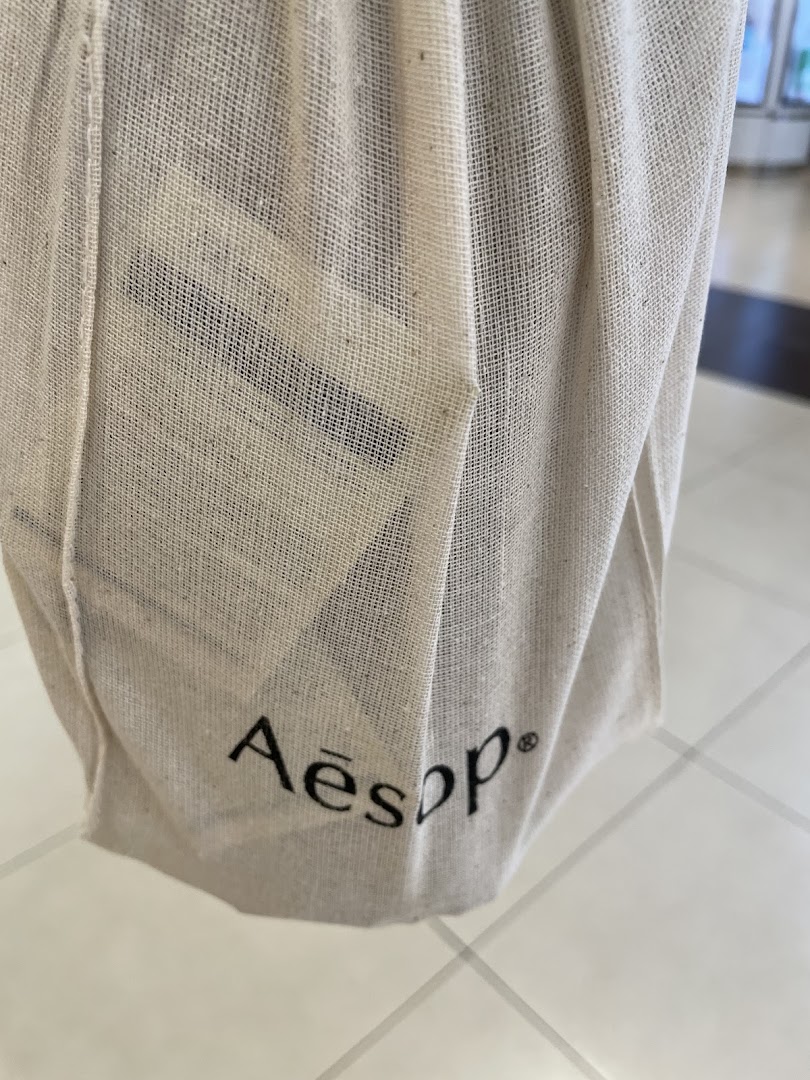 Close-up of a natural fabric Aesop branded reusable shopping bag.