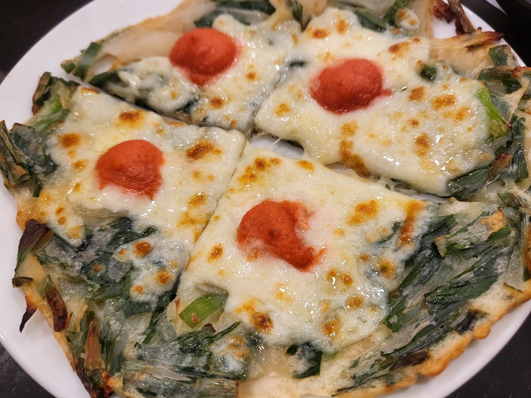 A close-up of a savory pancake topped with melted cheese and a red dollop, served on a white plate.