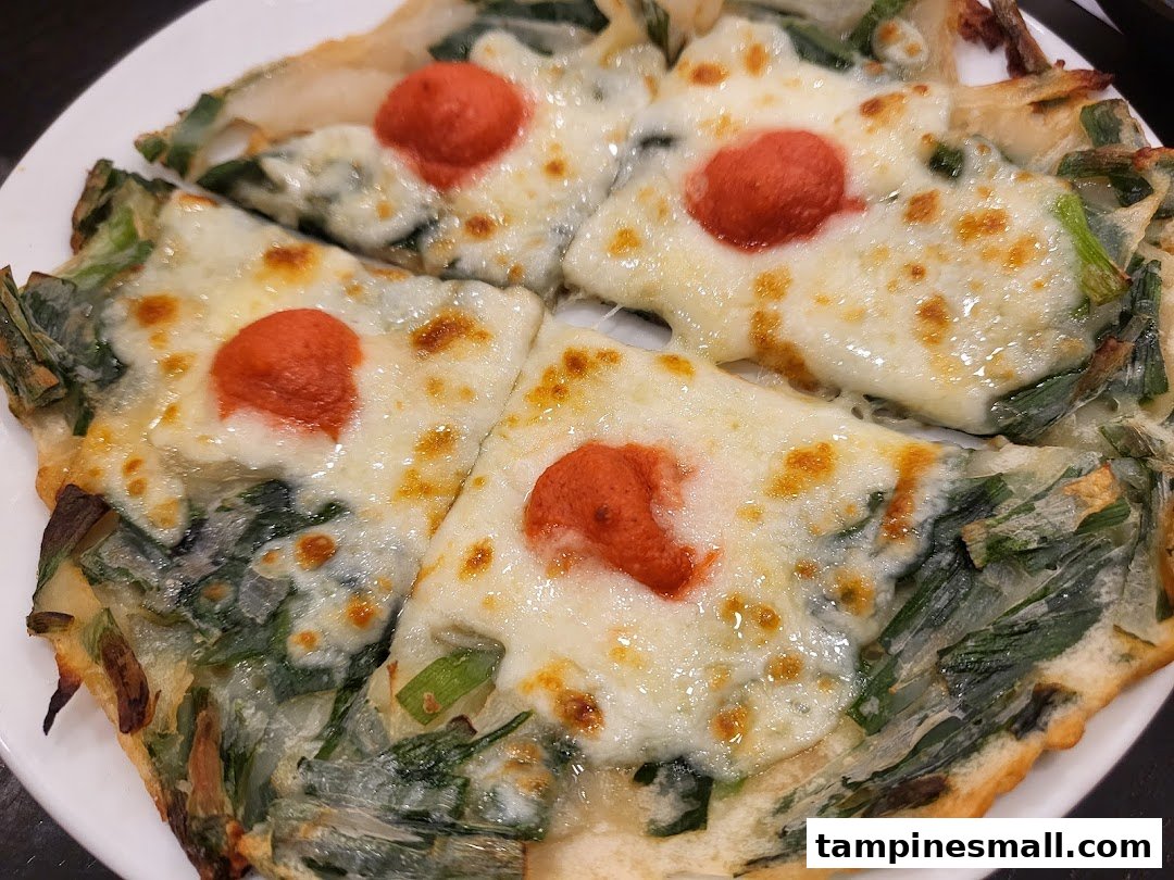 A close-up of a savory pancake topped with melted cheese and a red dollop, served on a white plate.
