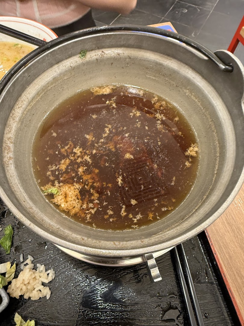 A close-up of a simmering hotpot or ramen broth in a metal pot at Ajisen Tanjiro.