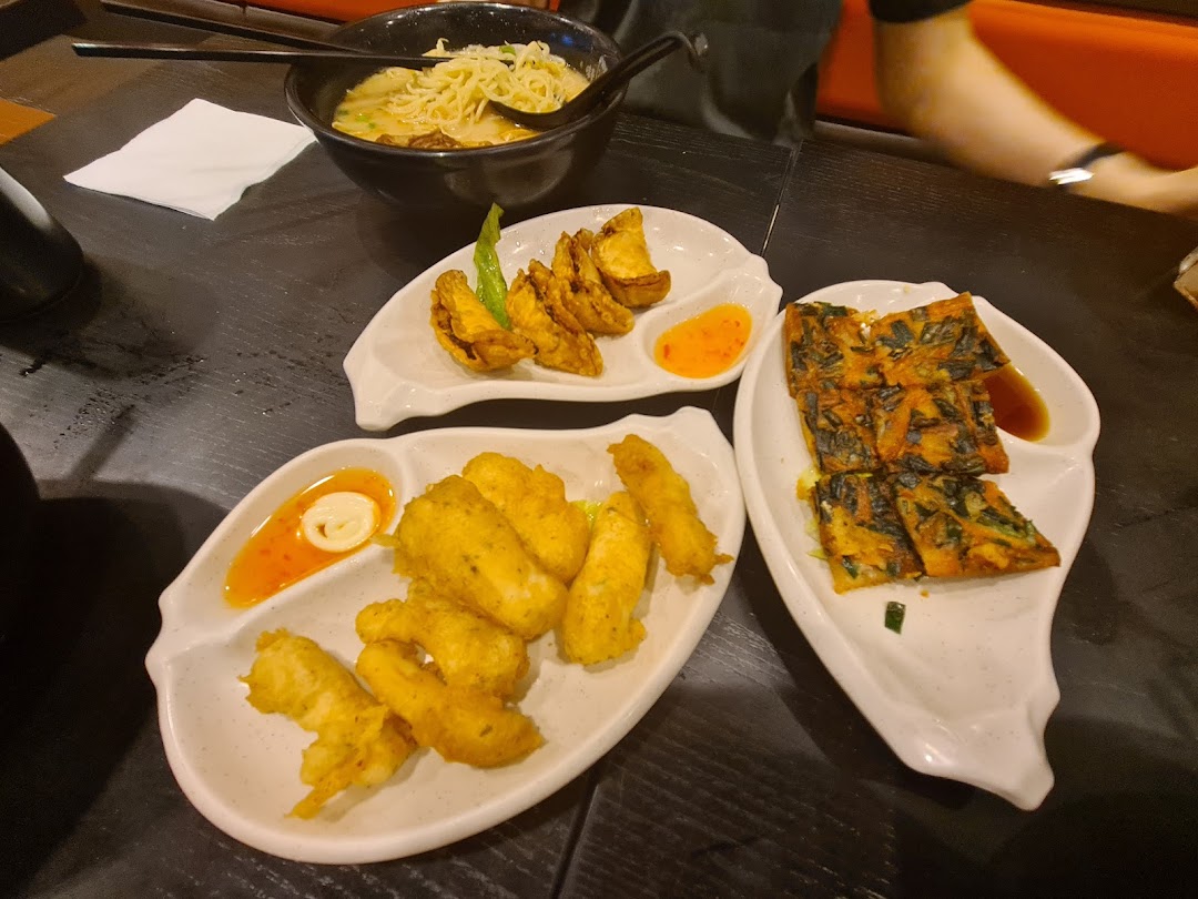 A table laden with a bowl of ramen, fried appetizers, and savory pancakes at Ajisen Tanjiro.