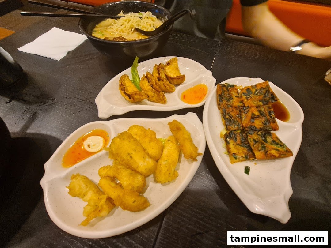 A table laden with a bowl of ramen, fried appetizers, and savory pancakes at Ajisen Tanjiro.