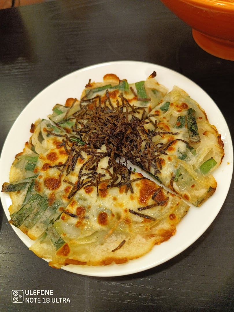 A savory pancake with green onions and a crispy topping, served on a white plate.