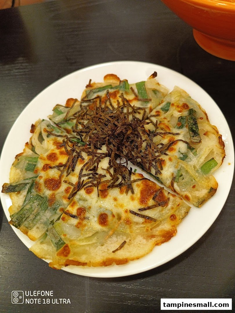A savory pancake with green onions and a crispy topping, served on a white plate.