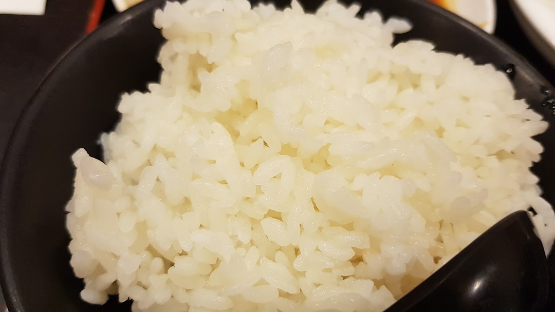 A close-up of a bowl of fluffy white rice with a black spoon, likely a side dish.