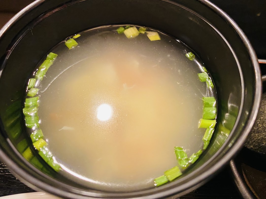 A close-up of a clear broth soup garnished with fresh green onions in a black bowl.