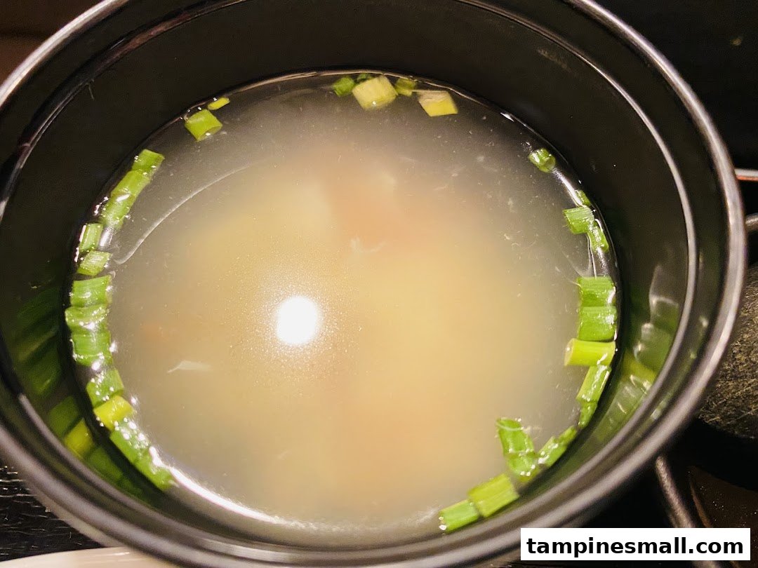 A close-up of a clear broth soup garnished with fresh green onions in a black bowl.
