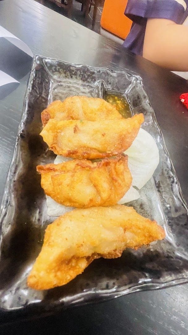 A plate of golden-fried dumplings with a dipping sauce, served on a dark textured dish.