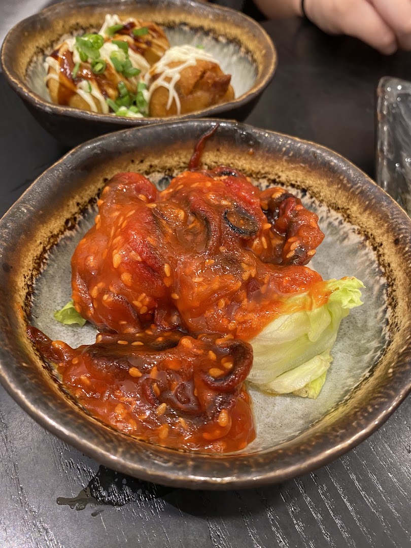 Two bowls of Japanese appetizers: spicy baby octopus and takoyaki, served in rustic ceramic bowls.