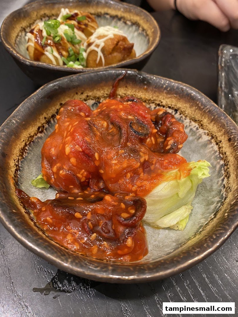 Two bowls of Japanese appetizers: spicy baby octopus and takoyaki, served in rustic ceramic bowls.