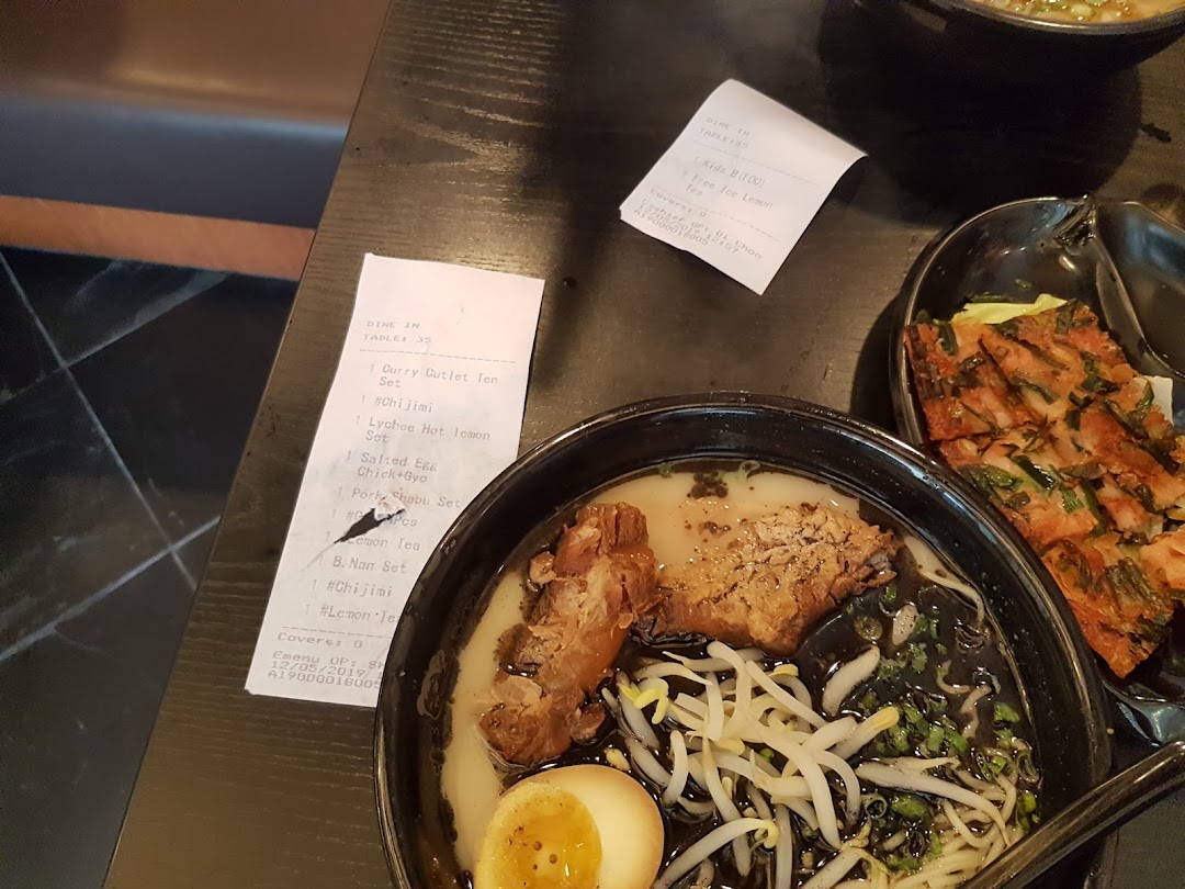 A close-up of a delicious ramen bowl with pork and a side dish on a dark table.