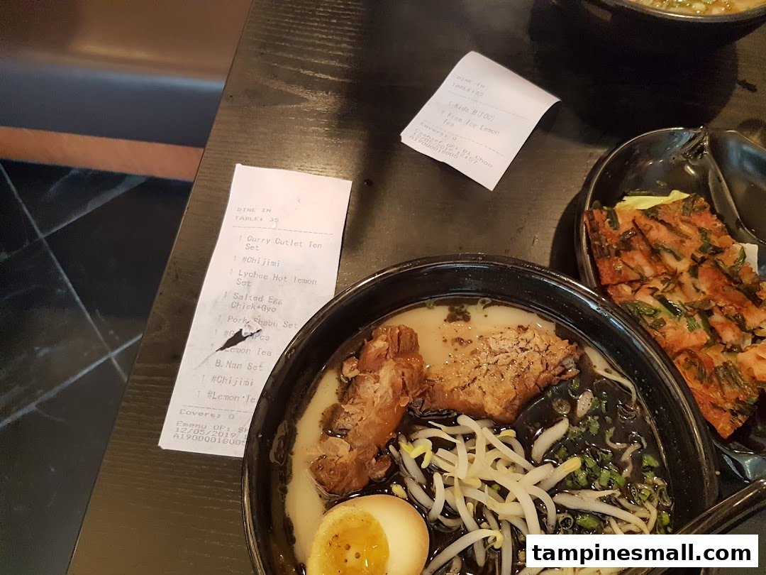 A close-up of a delicious ramen bowl with pork and a side dish on a dark table.
