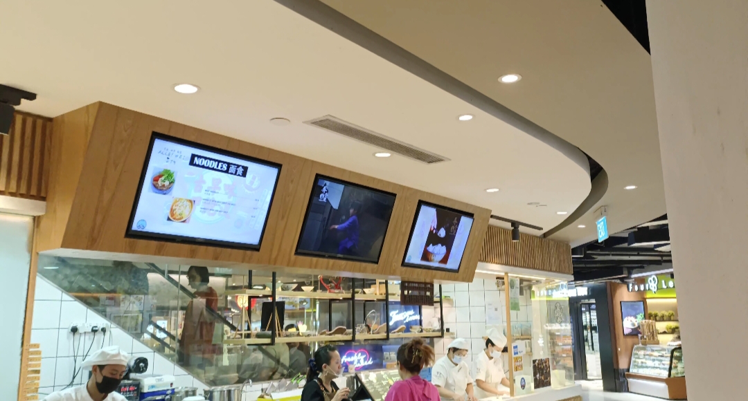 Staff prepare fresh noodles at Alley Wei's bustling food counter with digital menu displays.